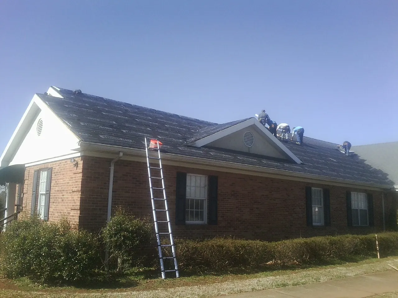 Crew tearing shingles off a brick ranch roof with a ladder set — Metal Roof Repair work by our crew in Los Banos