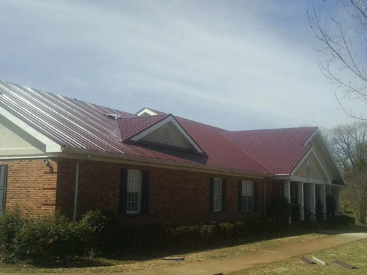 Red metal roof with gabled entries on a long brick building, from a Hail Damage Roof Repair job in Los Banos