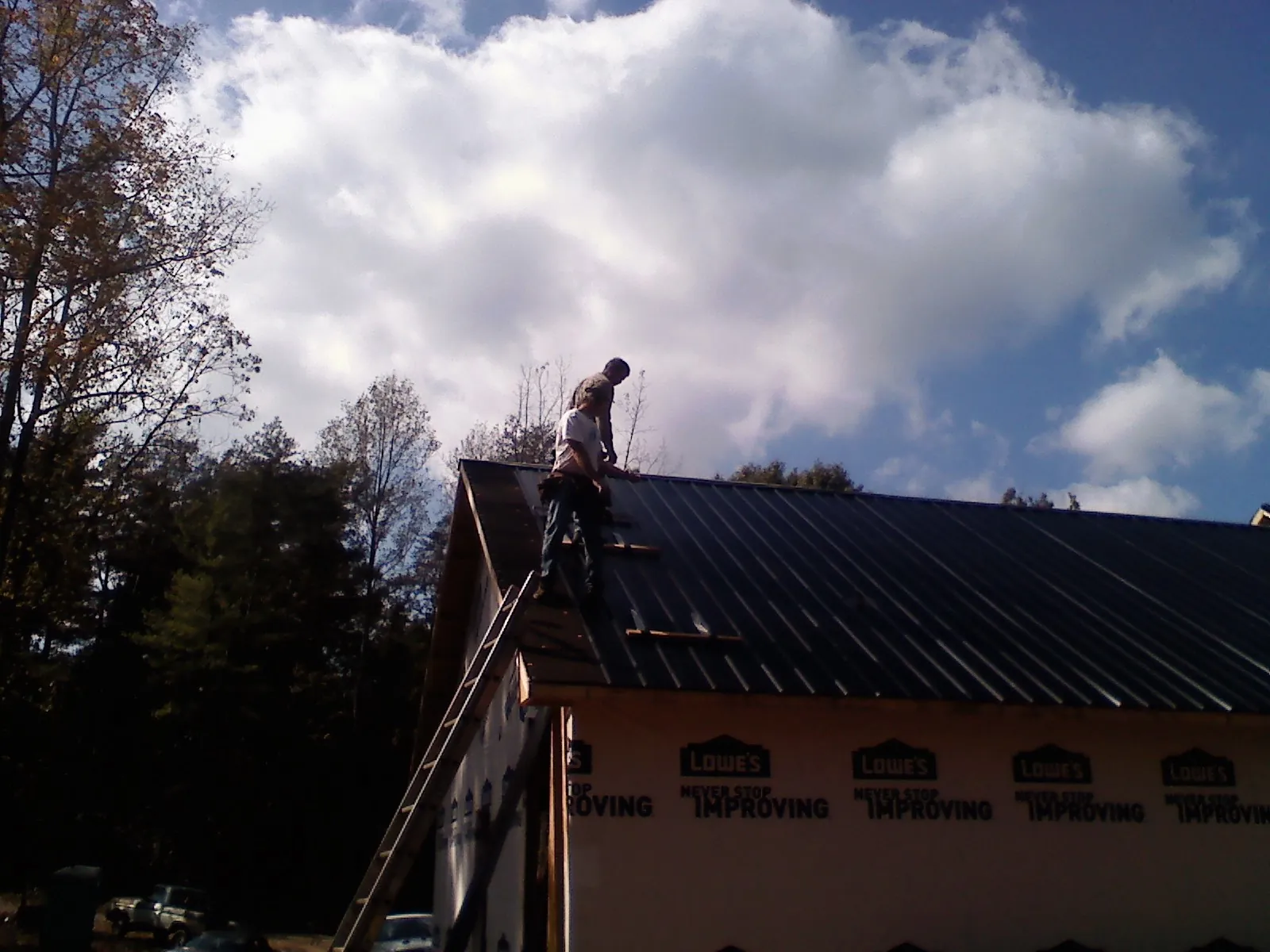 Roofer fastening dark metal panels high against a cloudy sky, from a Roof Inspection job in Los Banos