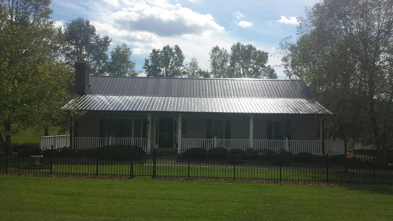 Gray metal roof on a brick ranch with a full width front porch — Gutter Guard Installation work by our crew in Los Banos