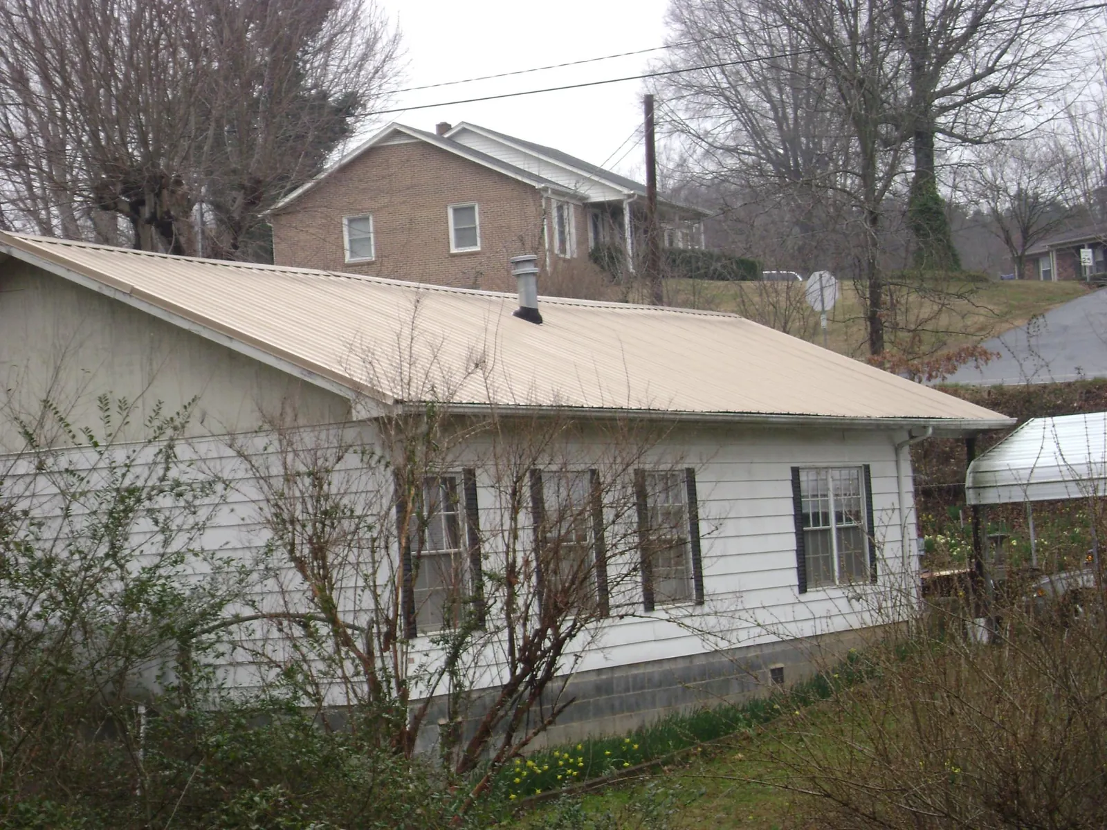 Tan metal roof on a white sided house set into a hillside — Commercial Roofing by Roofing Brothers in Los Banos
